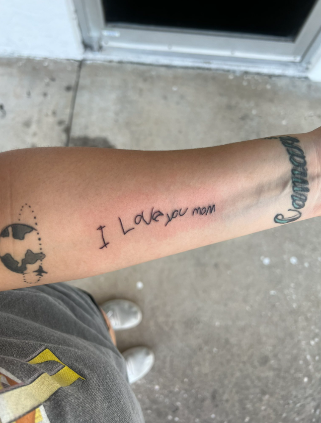 Close up of a woman's arm with a tattoo in her kid's handwriting that reads: I love you mom