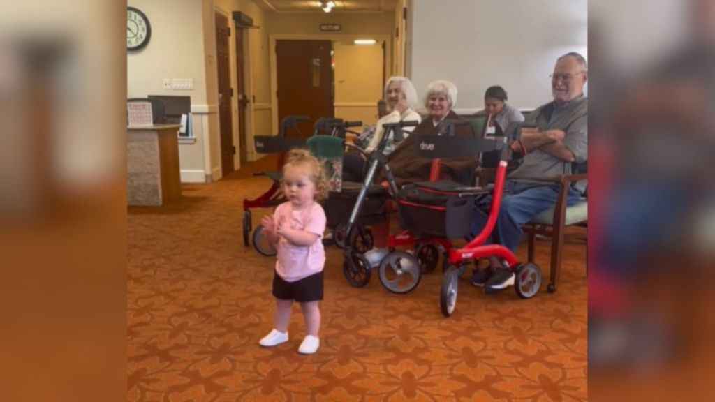 A little girl clapping her hands in a nursing home while listening to Ms. Rachel.