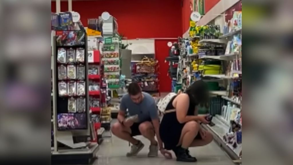 A peeping Tom places his phone underneath a crouching woman's skirt.