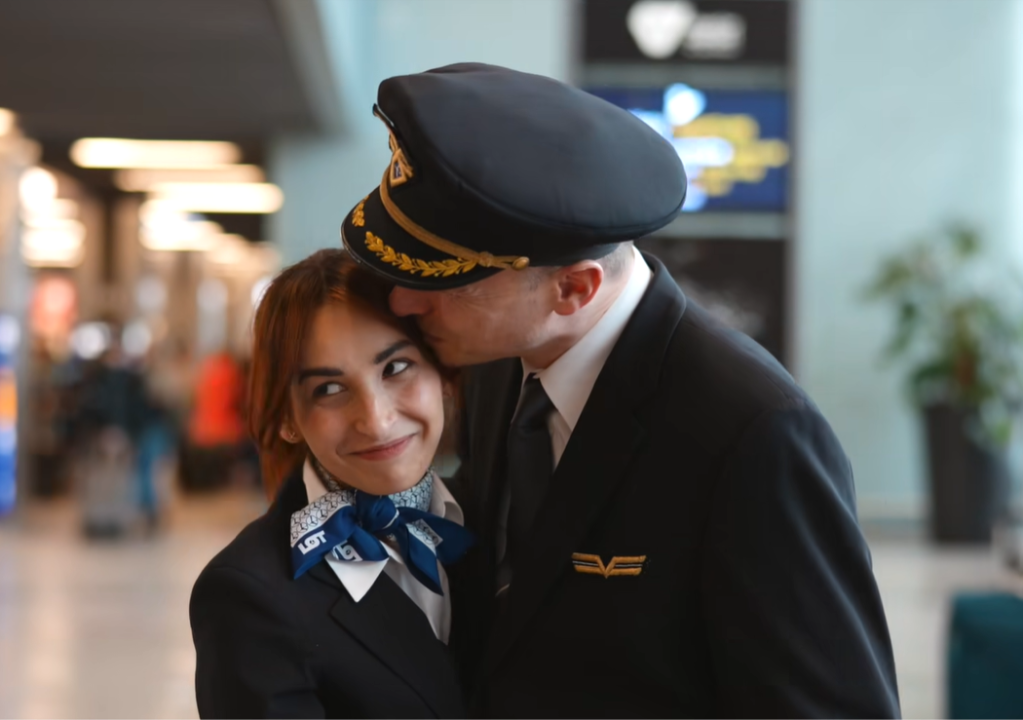 A pilot kisses the head of his flight-attendant fiancé who is smiling shyly as she looks up.