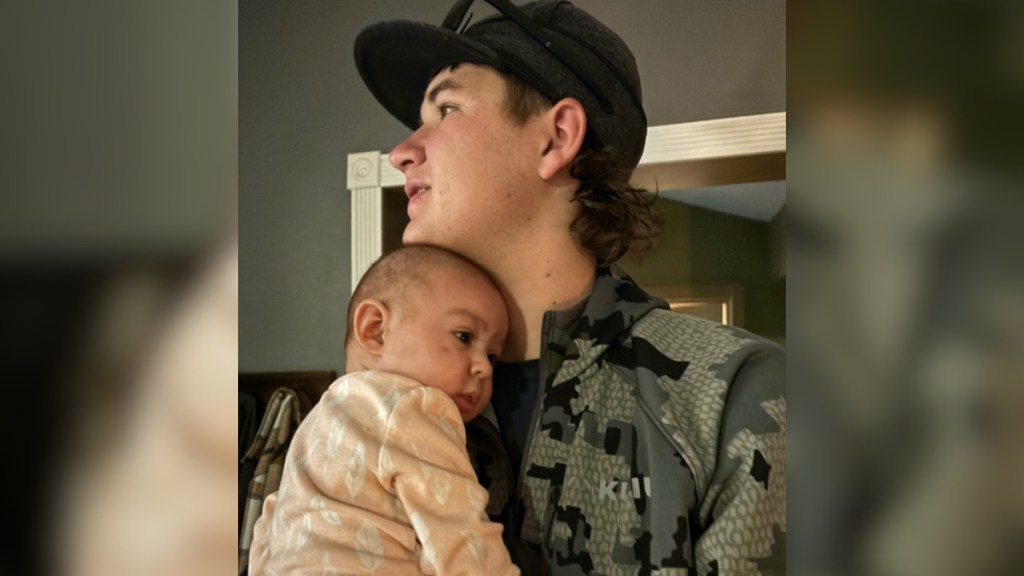 A man looks off into the distance as he holds a baby to his chest. The baby looks content.