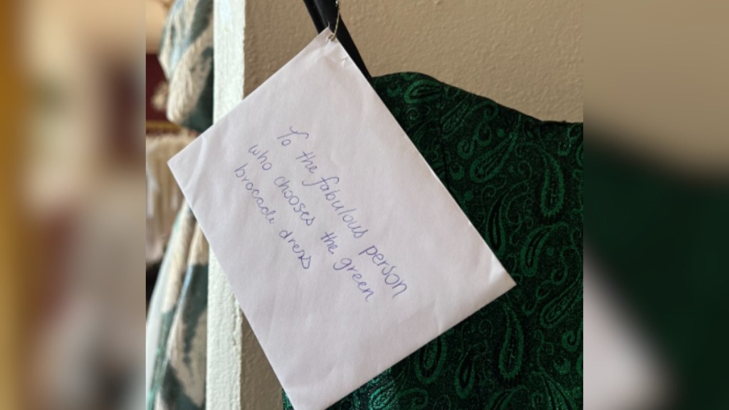 Close up of a green dress with an envelope attached. The envelope reads: to the fabulous person who chooses the green broccoli dress