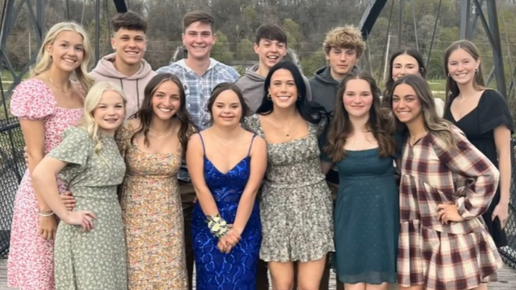 A teen with Down syndrome, Annie, poses in a sparkly blue dress outside with twelve friends before prom.