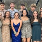 A teen with Down syndrome, Annie, poses in a sparkly blue dress outside with twelve friends before prom.