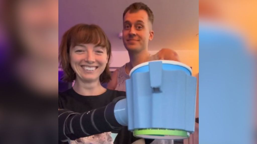 A woman with a prosthetic arm shows off her new attachment while her husband stands next to her.