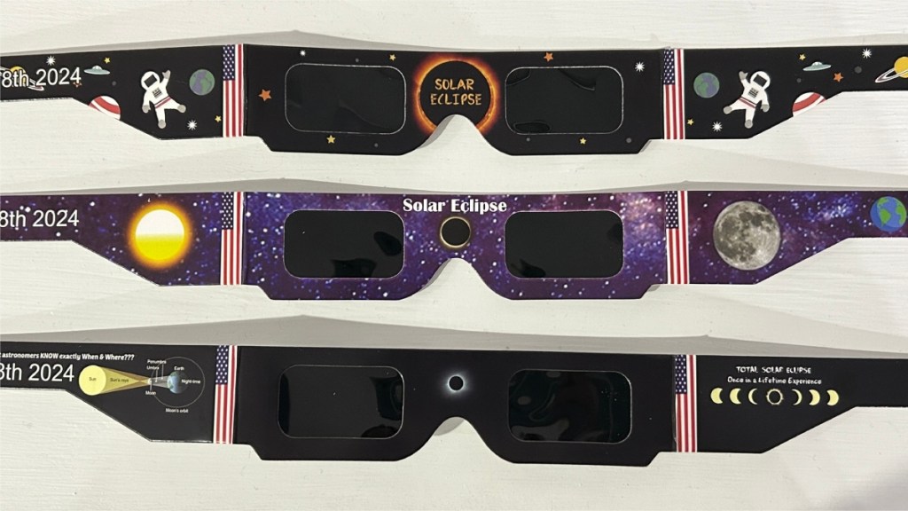 Row of three pairs of solar eclipse glasses laid out on a table