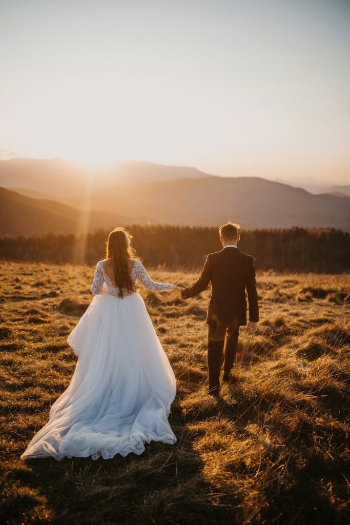 A bride and groom walking through a field.