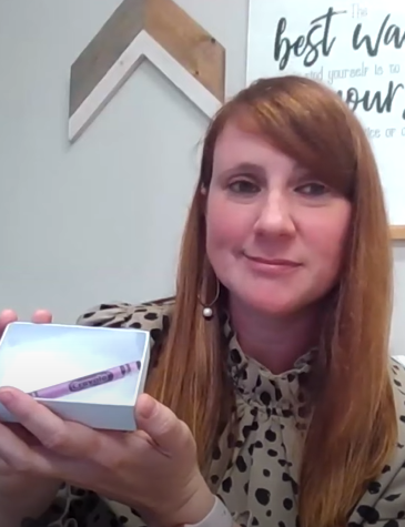 Heather smiles as she poses with a small box with a single, purple crayon inside.