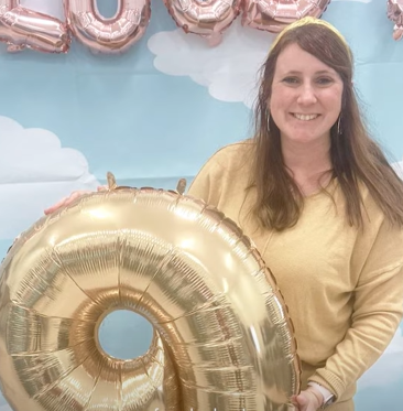 Heather Benoit smiles as she holds a "9" balloon.
