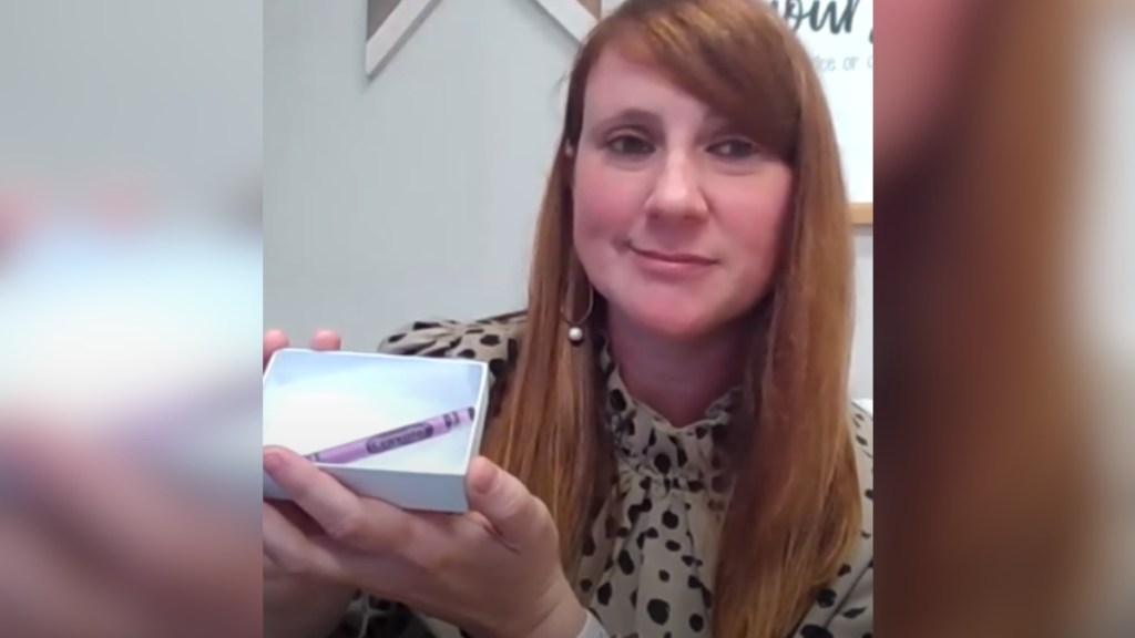 Heather smiles as she poses with a small box with a single, purple crayon inside.