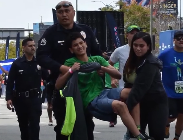 A police officer helps carry a boy across the marathon finish line.