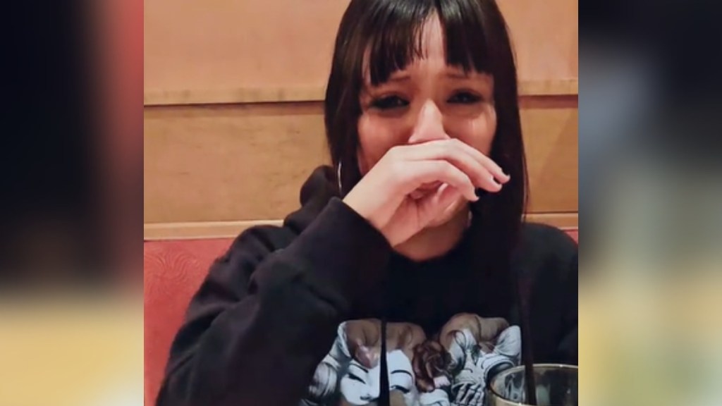 A teen covers her mouth with her hand as she starts to cry.