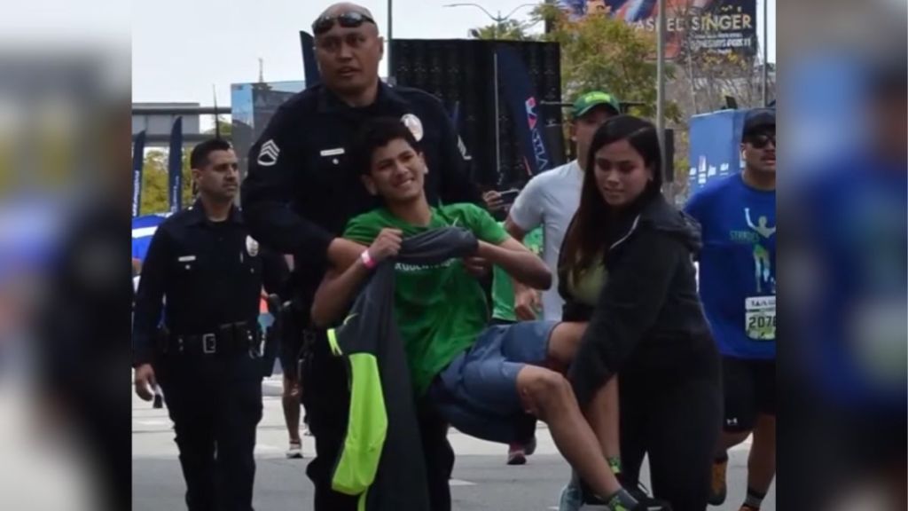 A police officer helps carry a boy across the marathon finish line.