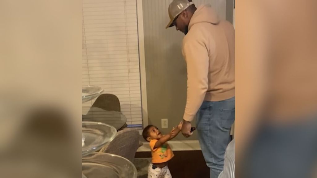 A toddler reaches up to be held when his dad walks through the door.