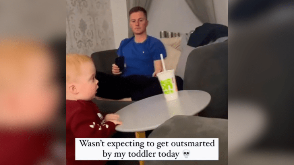 A toddler trying to grab Dad's soda cup from the table.