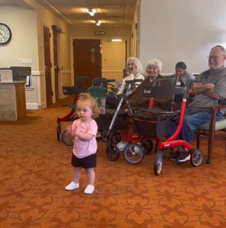 A little girl clapping her hands in a nursing home while listening to Ms. Rachel.