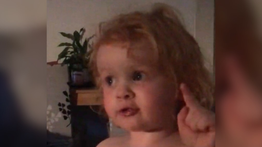 Close up of a toddler talking passionately. She's holding up a single finger as she does.