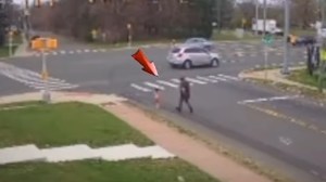 Security footage showing a road. A red arrow has been added to point out the small toddler running toward traffic. Behind her is a man trying to catch her.