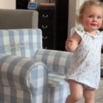 A toddler looks over at the camera as she starts to walk away from the toddler-sized chair she was sitting in.