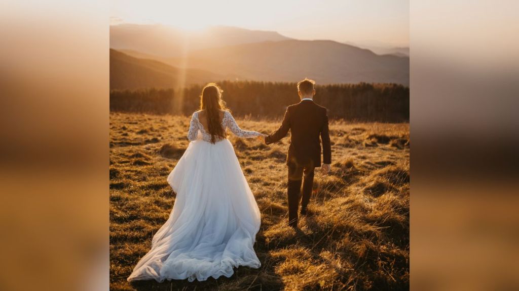 A bride and groom walking through a field.