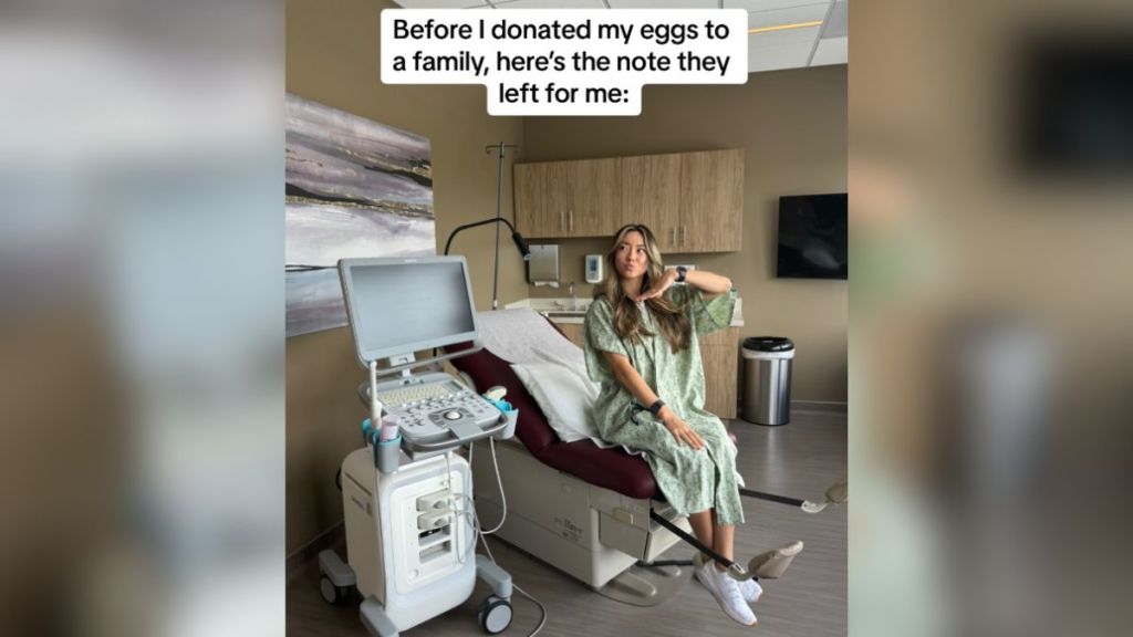 A young woman in a hospital gown sitting on an exam table.