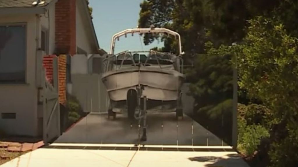 Image shows a boat mural on a fence that is an exact replica of the boat parked behind the fence.