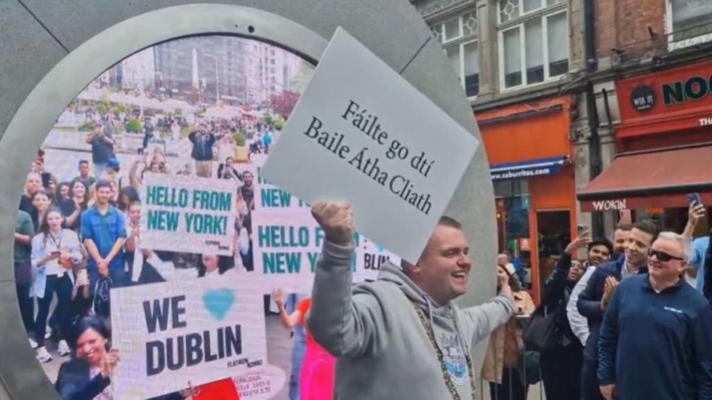 Image shows the virtual portal from Dublin, Ireland to New York with people holding up signs of welcome.