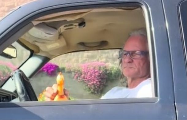 Man sitting in a green truck using a rubber chicken instead of road rage.