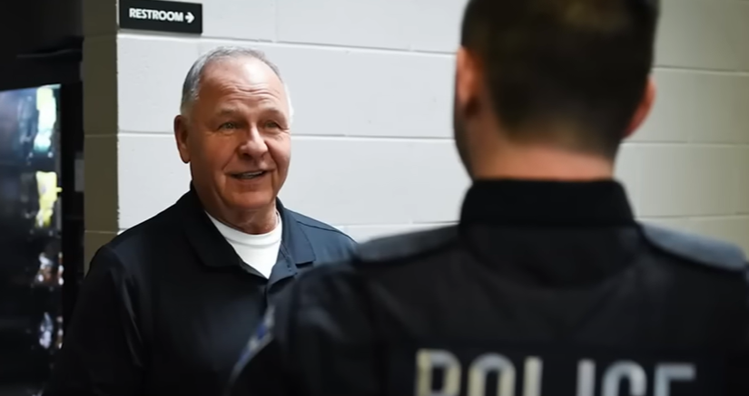 Gene Eyster smiles, mouth slightly open as he looks at a young man. He looks amazed to be looking at him. The young man's back is facing the camera.
