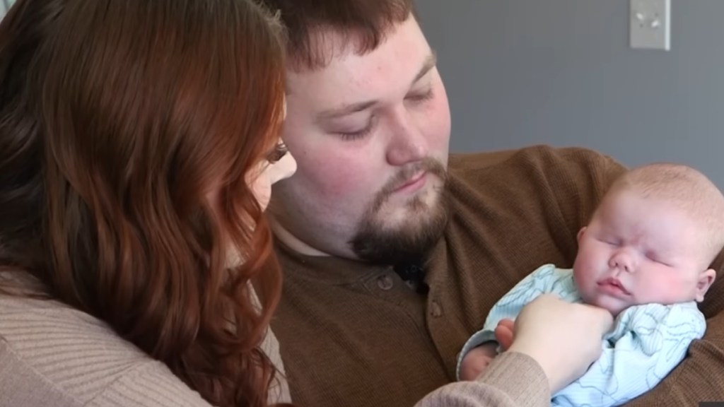 A woman and man smile as they look at their baby, Wrenley, who was born without eyes. Dad is holding the baby in his arms.