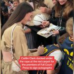 Celebrity athlete Caitlin Clark signing autographs at an event.