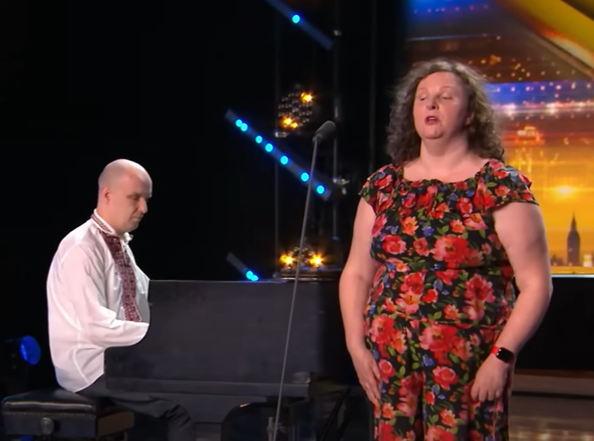 A woman sings on stage while her husband plays the piano.