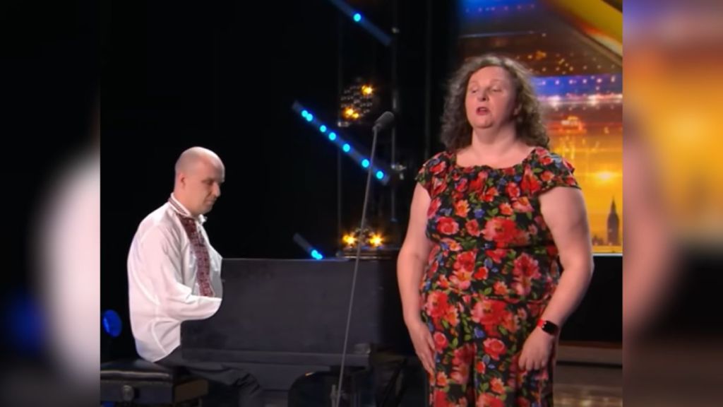 A woman sings on stage while her husband plays the piano.