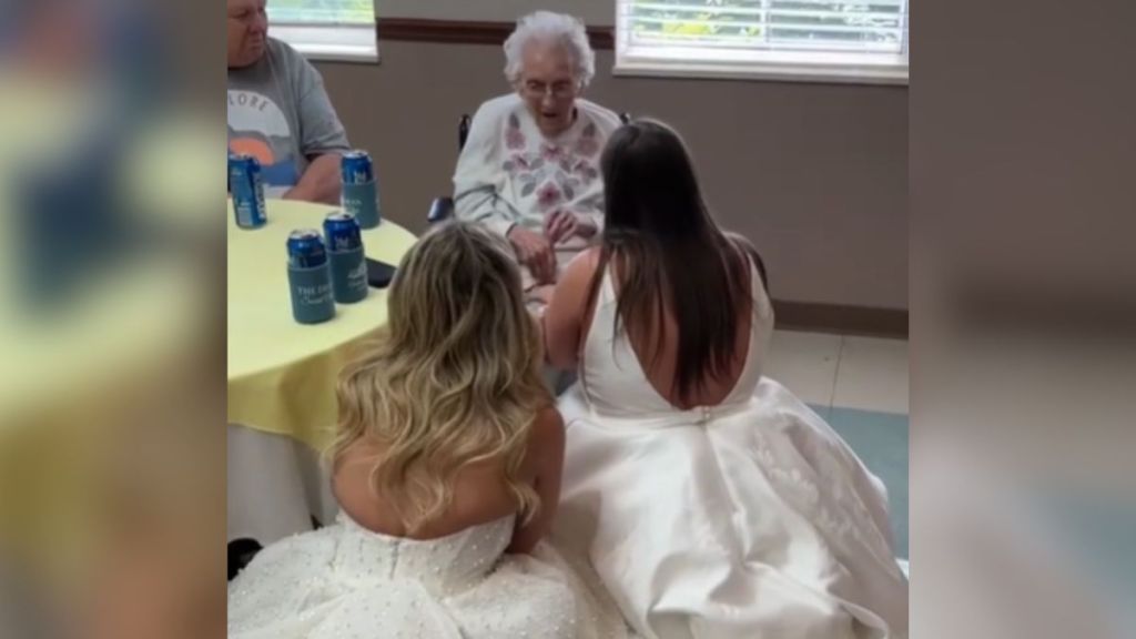 Two brides dressed in white kneeling in front of their great-grandma.