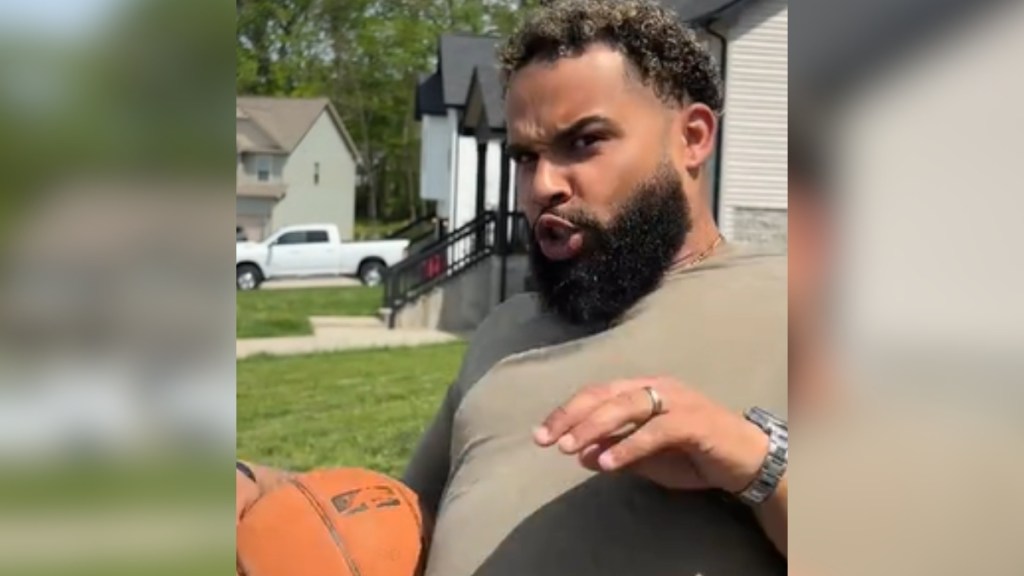 A man looks amazed as he stands outside, basketball under one arm.