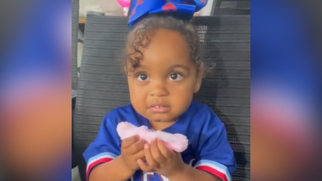 A little girl holds a piece of cotton candy in her hands, looking unsure