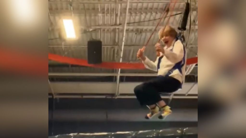 An excited elderly woman riding an indoor zip line.