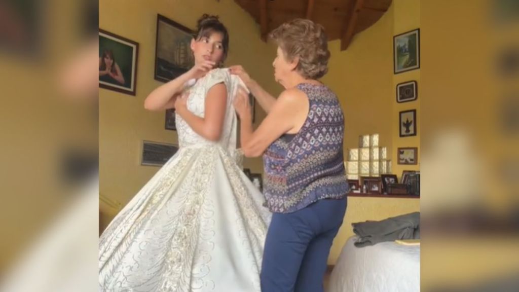An older woman helps a young woman into a white prom dress.
