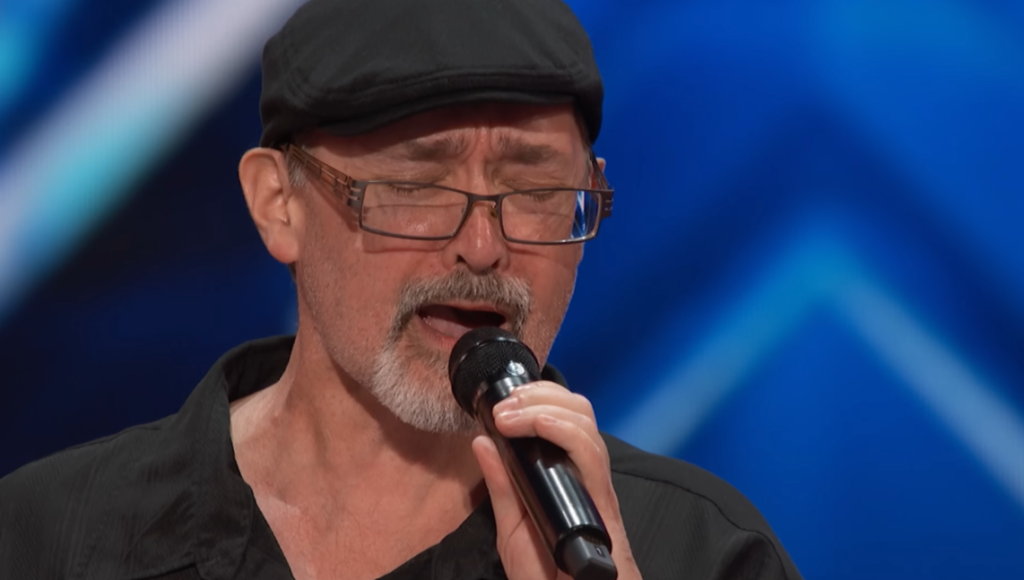 Close up of Richard Goodall singing passionately with his eyes closed.