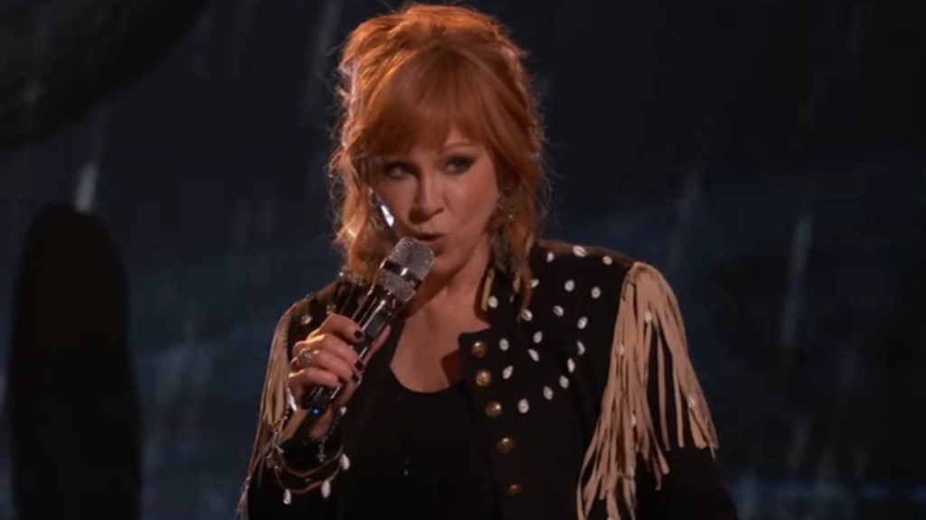 Reba looks serious as she sings into a mic on "The Voice."