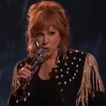 Reba looks serious as she sings into a mic on "The Voice."