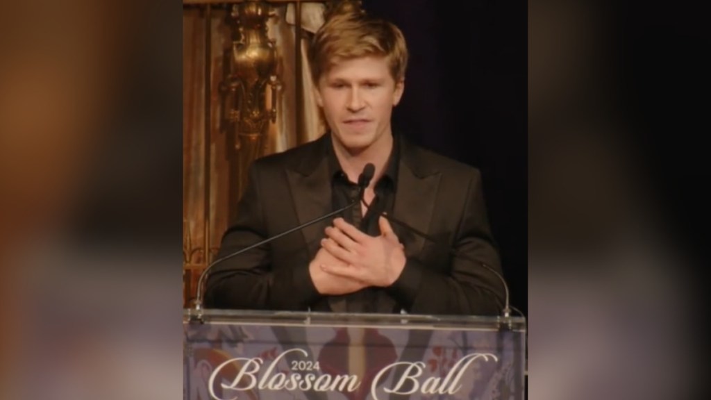 Robert Irwin places his hands on his chest as he speaks at a podium which reads "Blossom Ball."