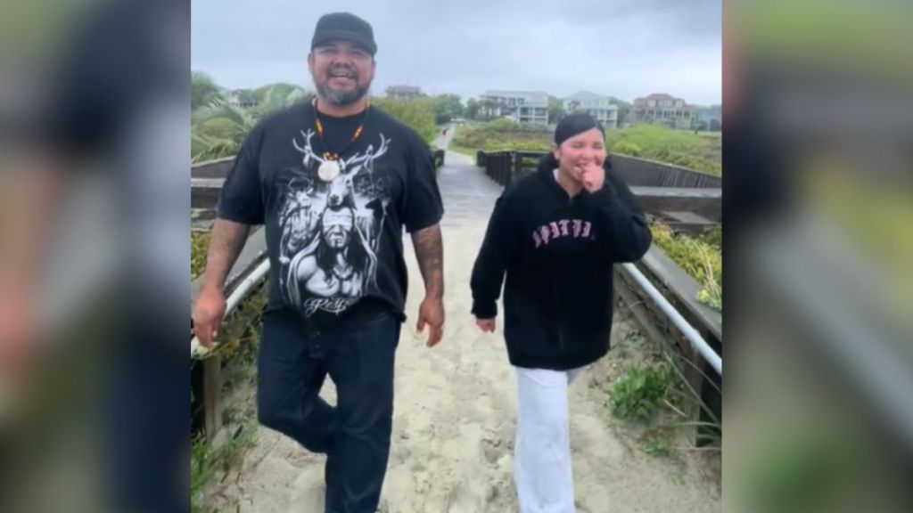 A smiling man and an emotional woman walking toward the ocean.