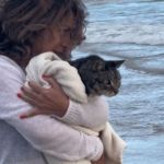 A woman holds her cat at the beach so he can see the ocean.