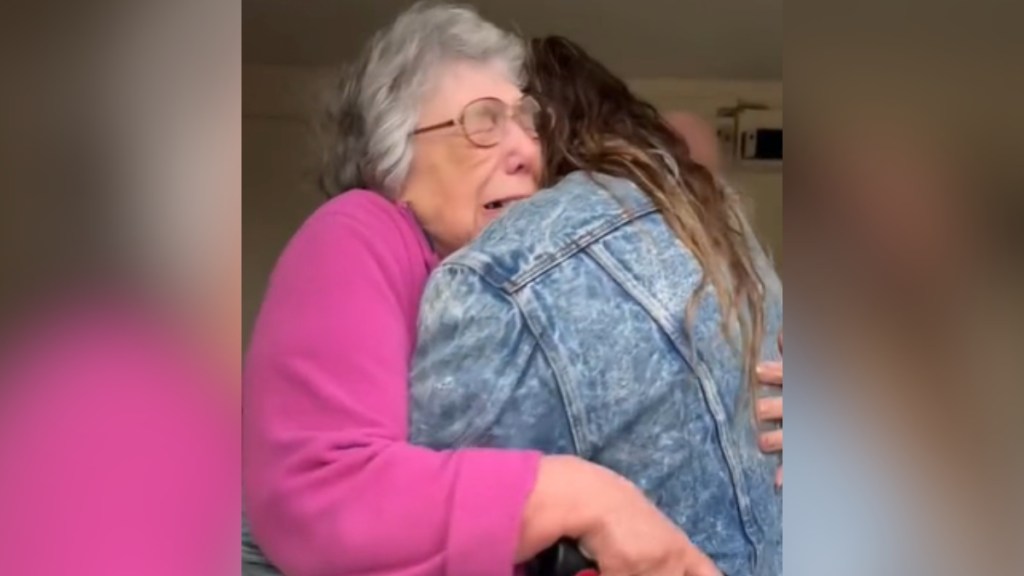 An elderly woman cries tears of joy, eyes closed, as she hugs a woman tightly.