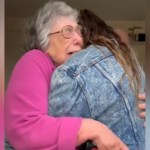 An elderly woman cries tears of joy, eyes closed, as she hugs a woman tightly.