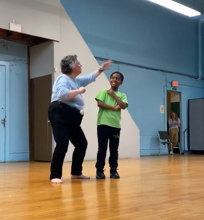 A young boy smiles as a woman dances next to him