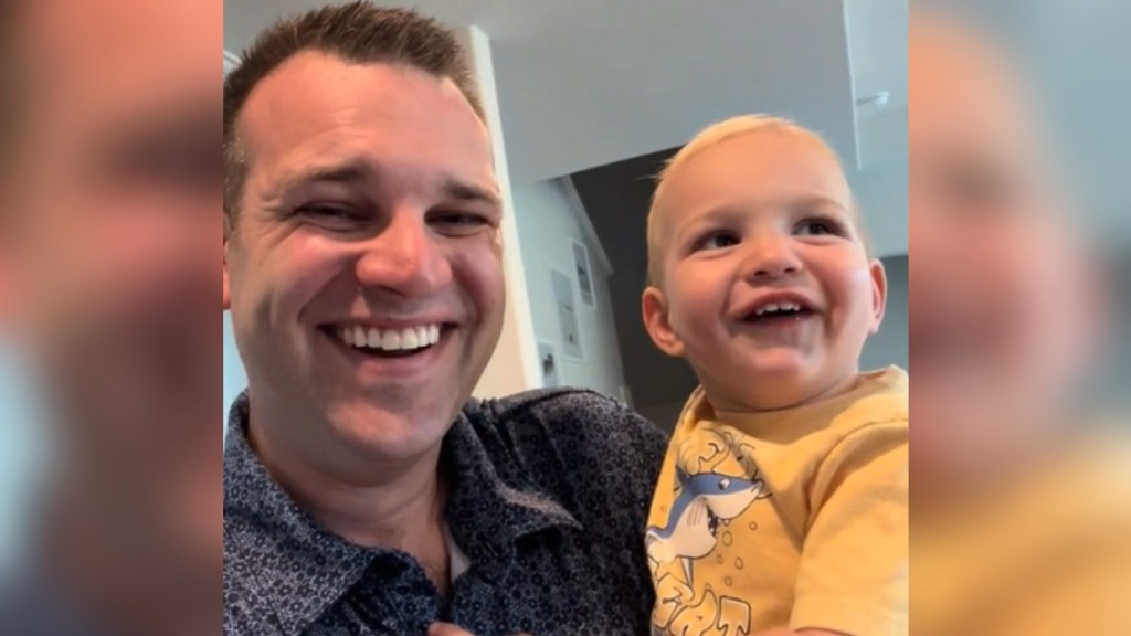 Close up of a man laughing as he holds his laughing toddler.