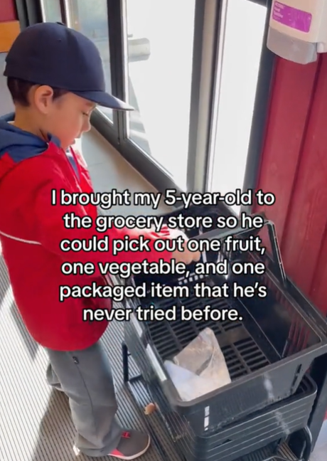 A little boy picks up a basket at the grocery store.