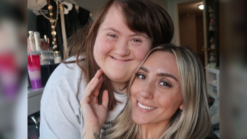 A blonde woman and her sister with Down syndrome smiling.